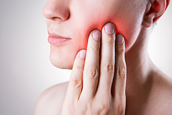 digitally enhanced close up of a patient putting her hand up to her jawline where there is a red and swollen area that might be a sign of infection