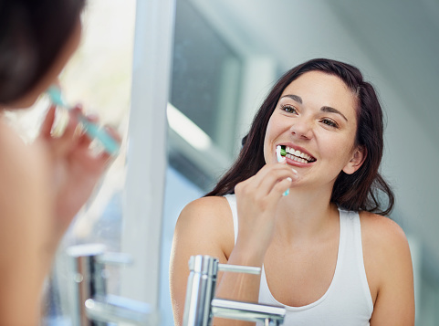  female patient brushing teeth gently in the mirror