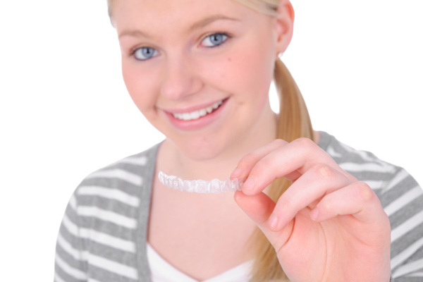 Teenage girl holding her clear aligner after bite adjustment at Singing River Dentistry in Muscle Shoals, AL