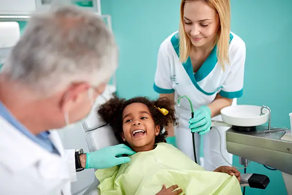 adorable kid in the dental chair smiling at the dentist and dental assistant by her side