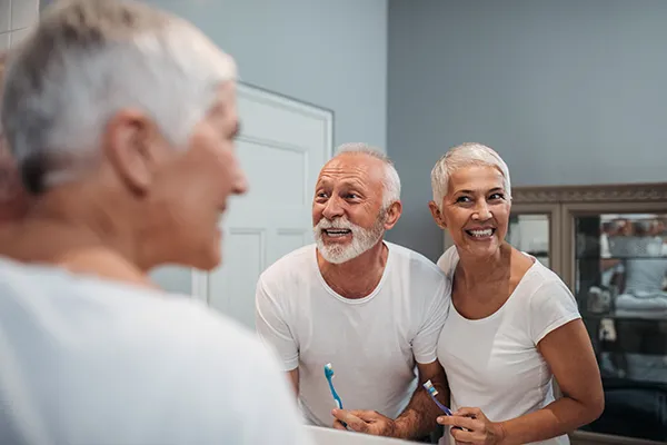 mature white couple smiling and brushing their teeth in the bathroom mirror