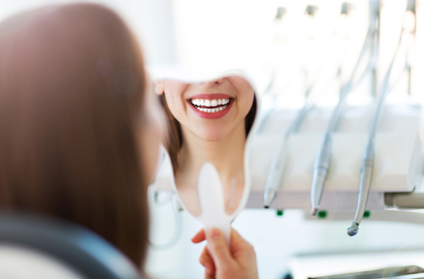  Woman looking at her smile in a mirror after dental implant treatment at Singing River Dentistry.