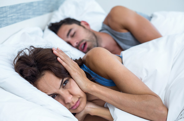 A woman covering her ears as husband with sleep apnea snores at Singing River Dentistry in Muscle Shoals, AL