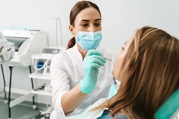 A dentist wearing a face mask examining a female patient's teeth during a dental visit in a clinic.