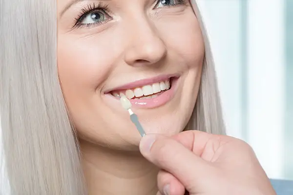 Dentist holding a dental veneer shade guide next to a smiling patient's teeth to match the perfect color for veneers.