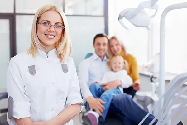 A female dentist smiling and standing in front of a family sitting in the dentist chair, representing another successful dental visit.