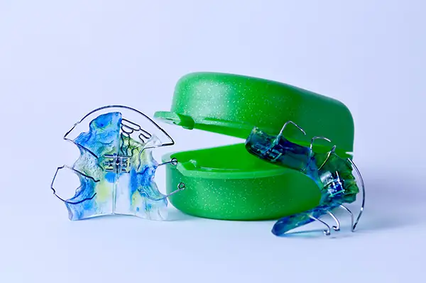 Two colorful wire and plastic retainers placed next to a retainer case on a white background.